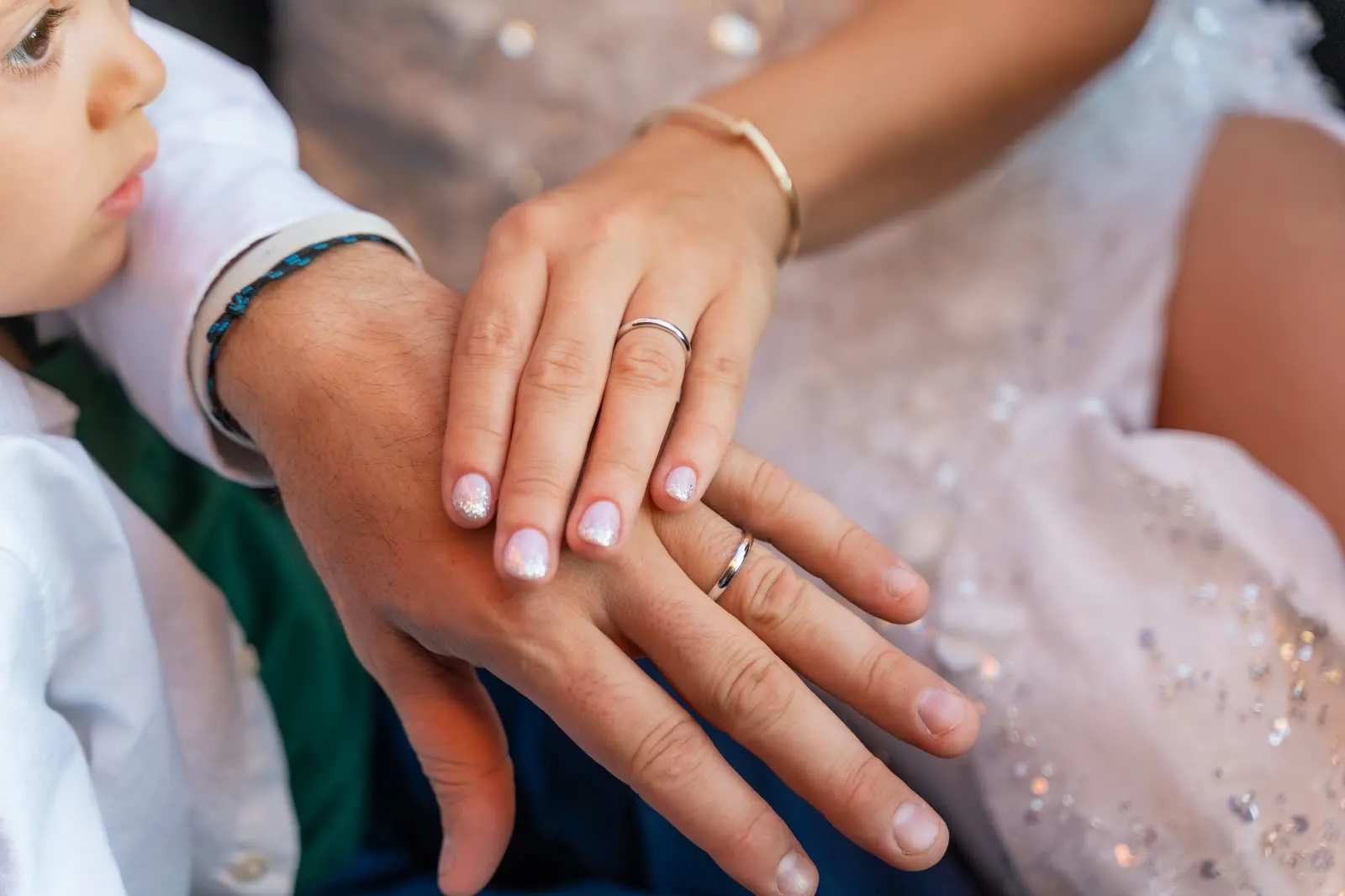 Le mani degli sposi una sopra l'altra, con le fedi in primo piano e il volto di un bambino accanto