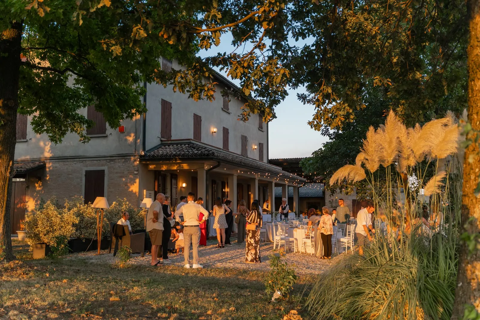 Gli invitati chiacchierano nel giardino del ricevimento davanti alla casa, nella luce dorata del tramonto, con le pampas in primo piano