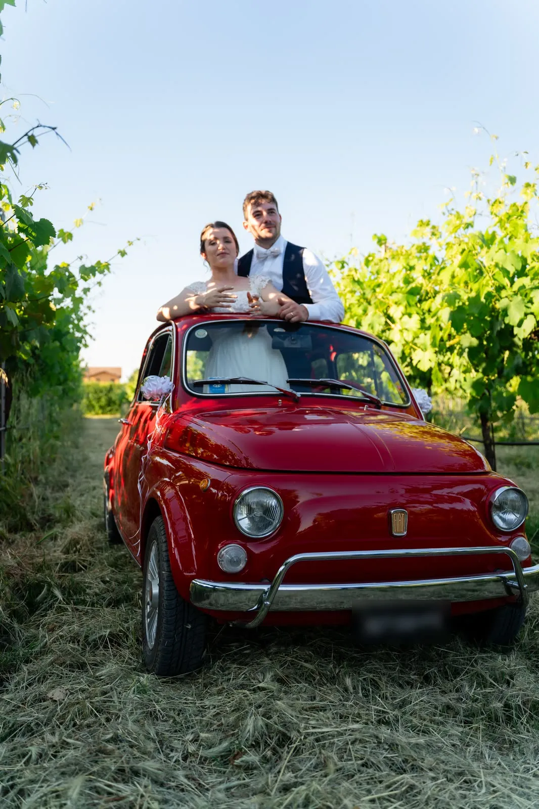 Gli sposi in piedi nell'abitacolo della Fiat 500, con il tettuccio aperto, in mezzo alla vigna