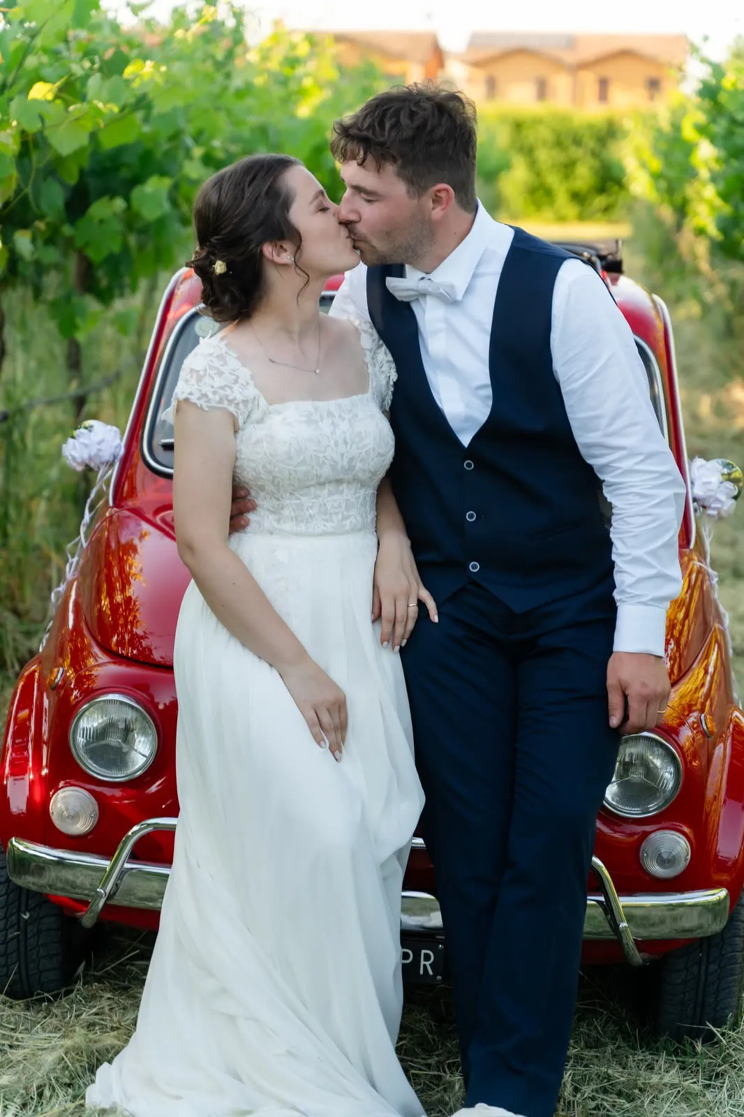 Gli sposi si baciano appoggiati al cofano della Fiat 500 rossa, in mezzo alla vigna