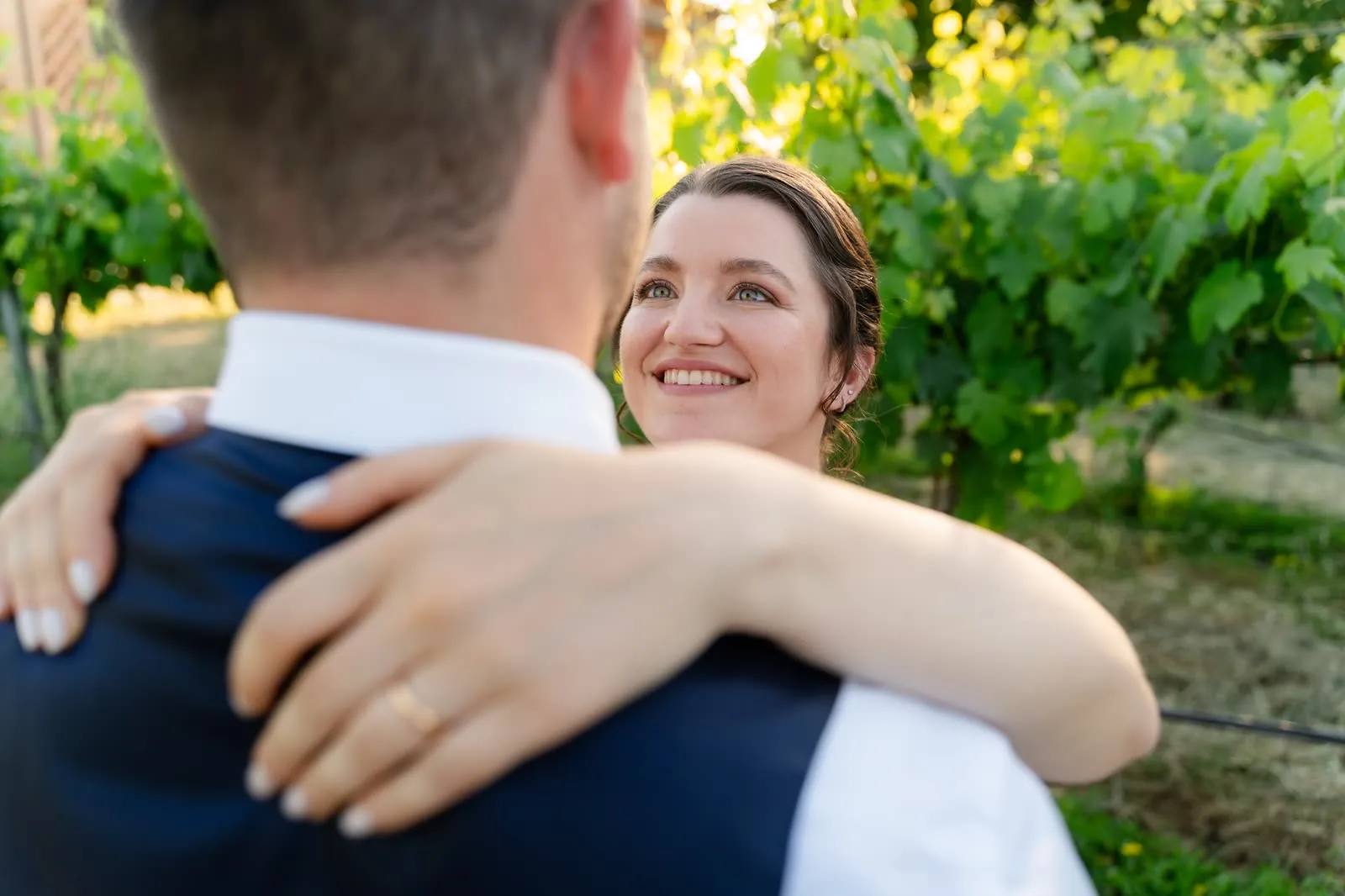 La sposa sorride guardando lo sposo, con il braccio intorno alle sue spalle e la fede in primo piano