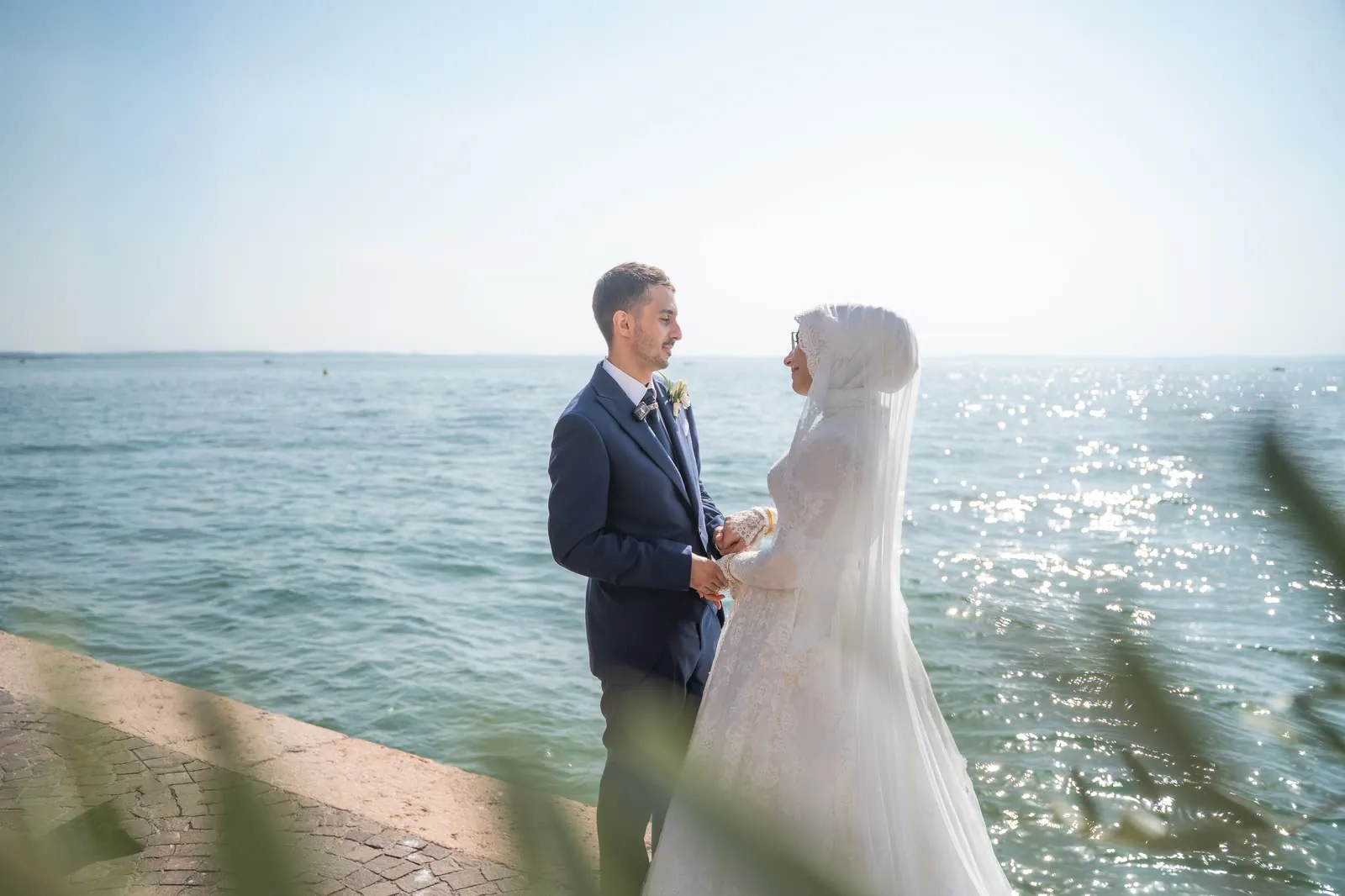 Gli sposi si guardano tenendosi per mano sul lungolago di Lazise, con il Lago di Garda che scintilla alle spalle