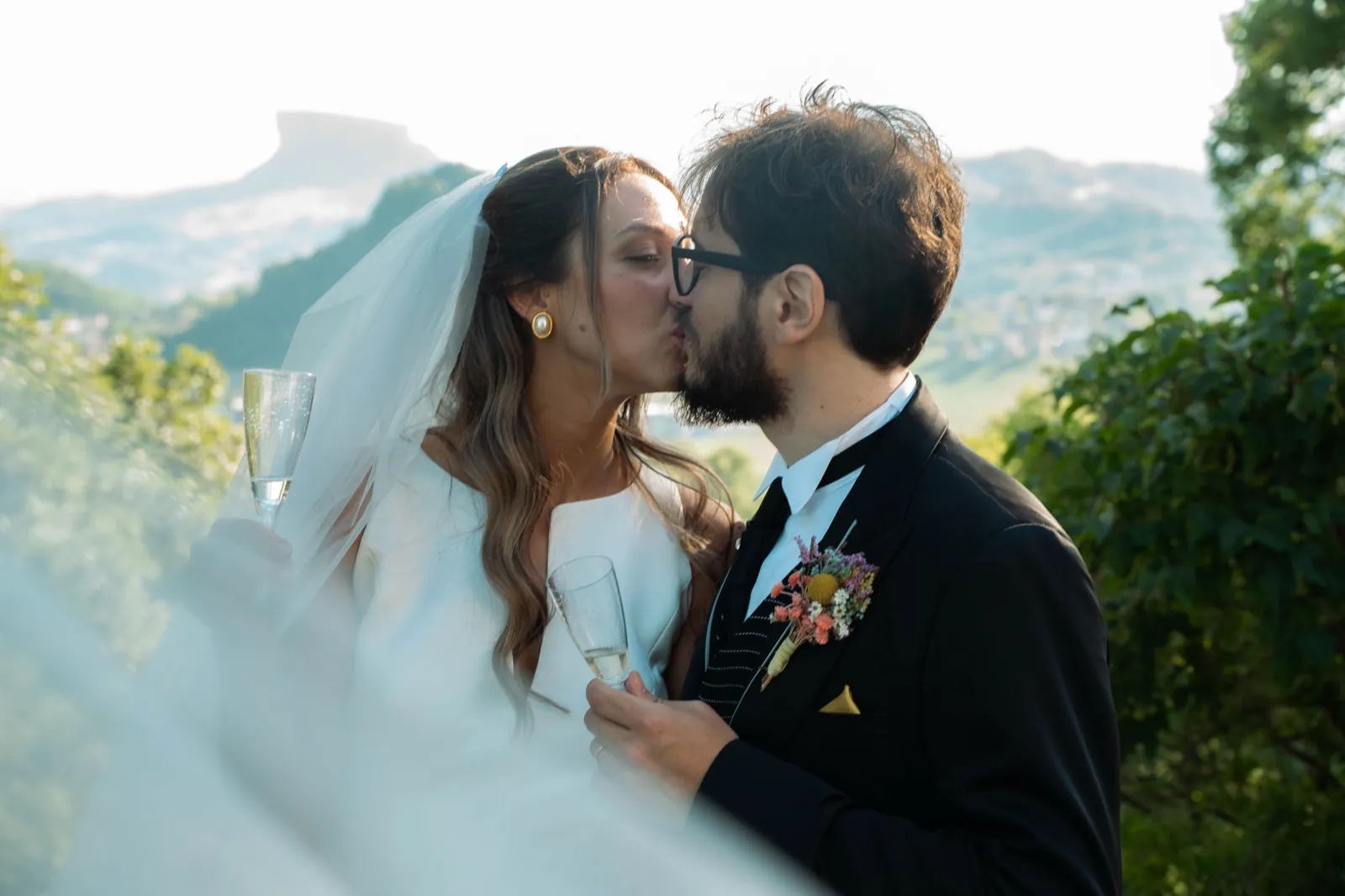 Gli sposi si baciano con la Pietra di Bismantova sullo sfondo, calici in mano
