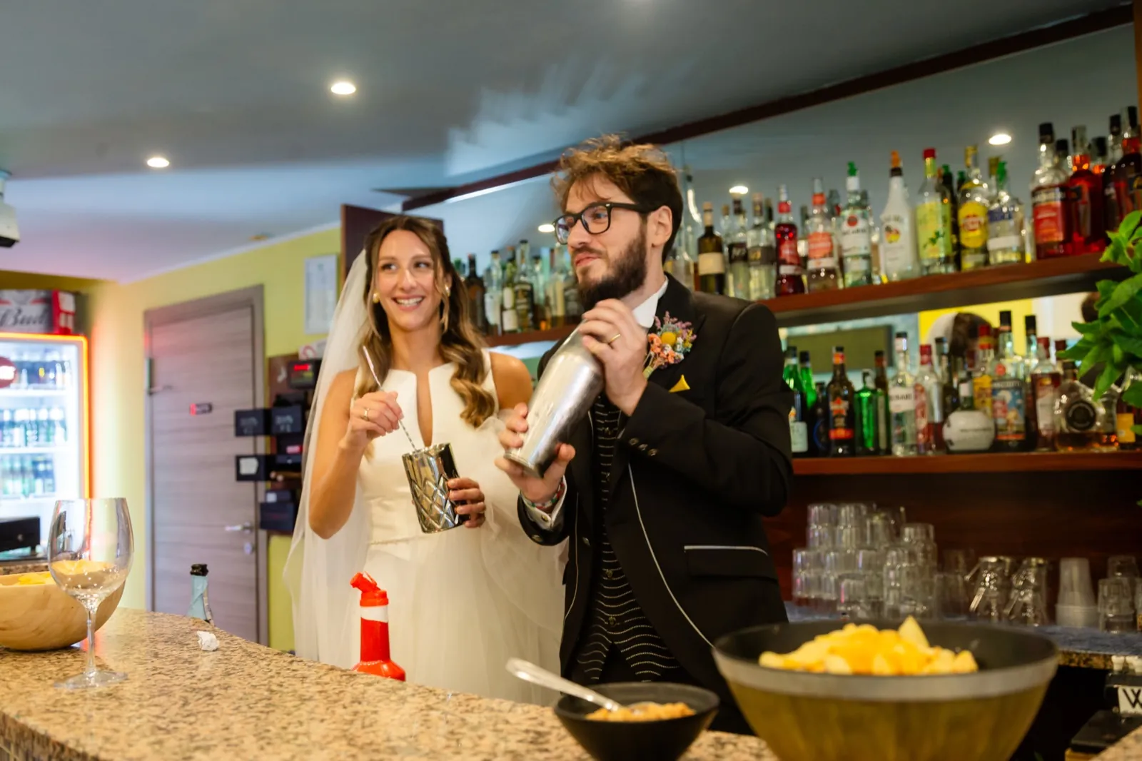 Maria e Simone, sposi a Casina, preparano cocktail dietro il bancone di un bar nella sosta tra cerimonia e ricevimento