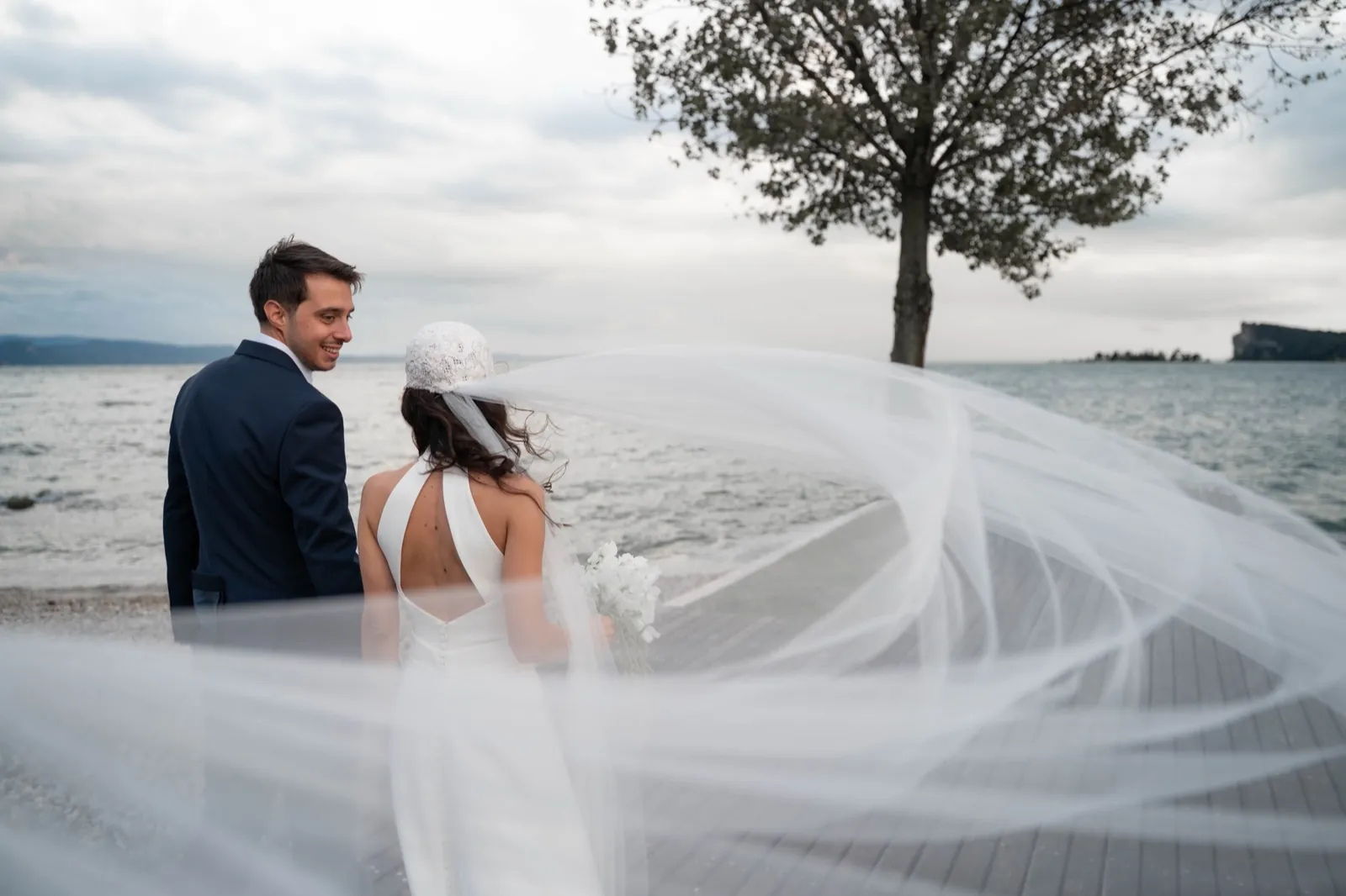 Gli sposi camminano su un pontile di legno sul Lago di Garda, il velo mosso dal vento