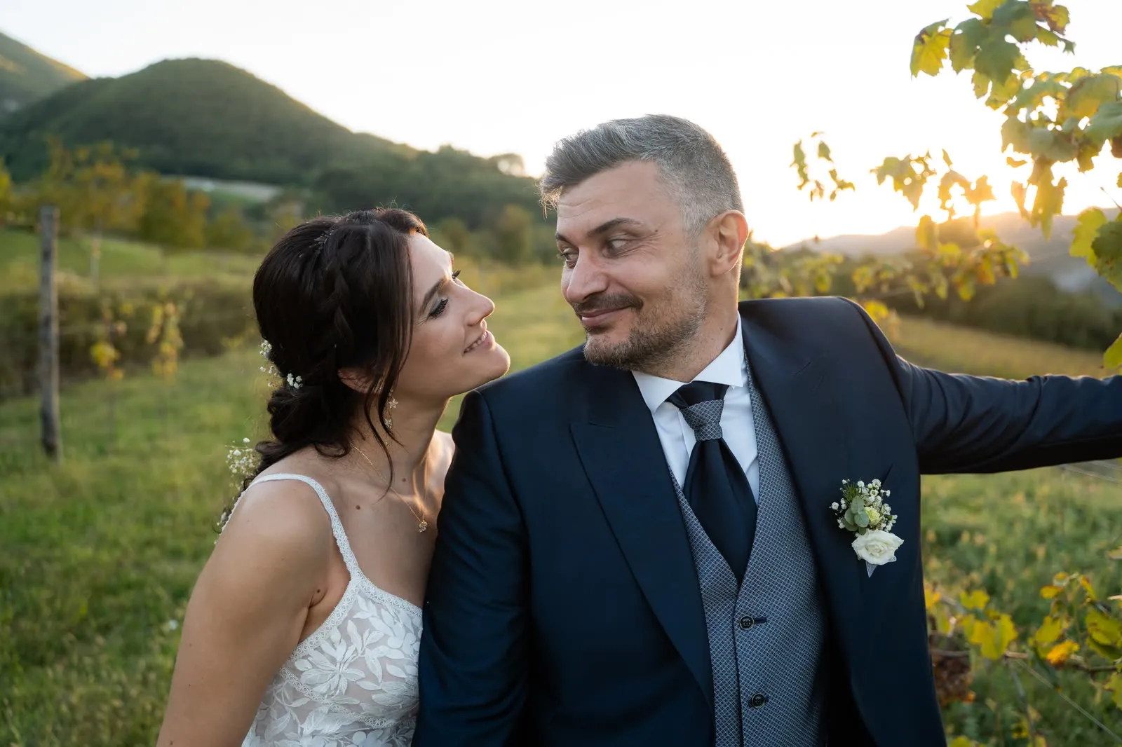Gli sposi si guardano sorridendo tra le vigne al tramonto, lei con la testa appoggiata alla spalla di lui